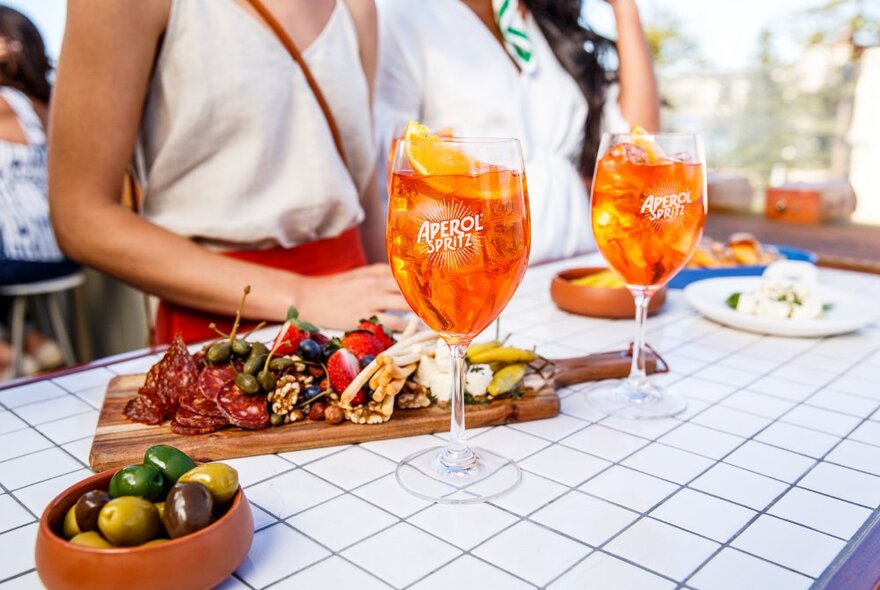 Trays of food and spritz Aperol cocktails on an outdoor dining table.