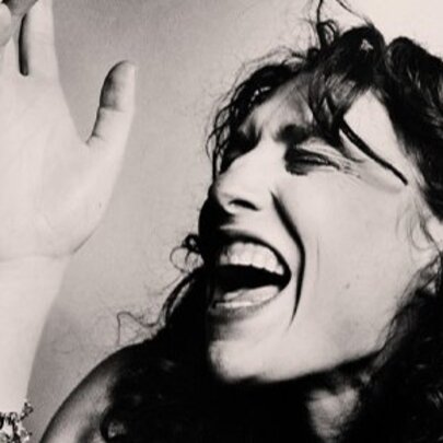 Woman singing, her eyes shut and hand raised.