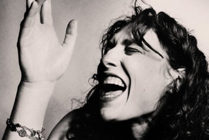 Woman singing, her eyes shut and hand raised.