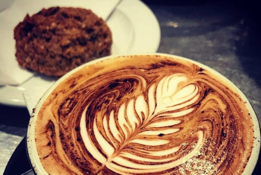 Close up of cappuccino with biscuit on a plate in the background.