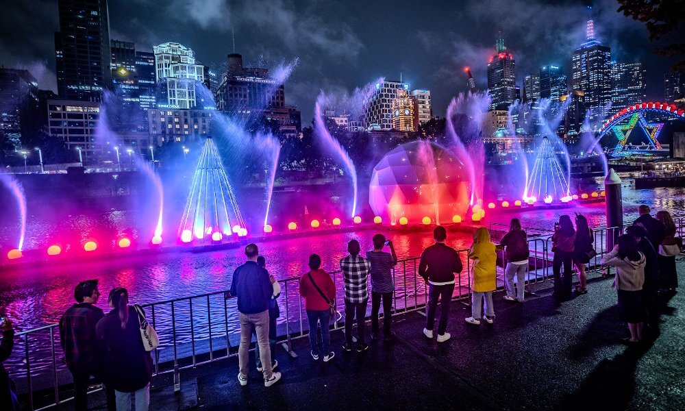 Crowds watching a colourful river show at night.