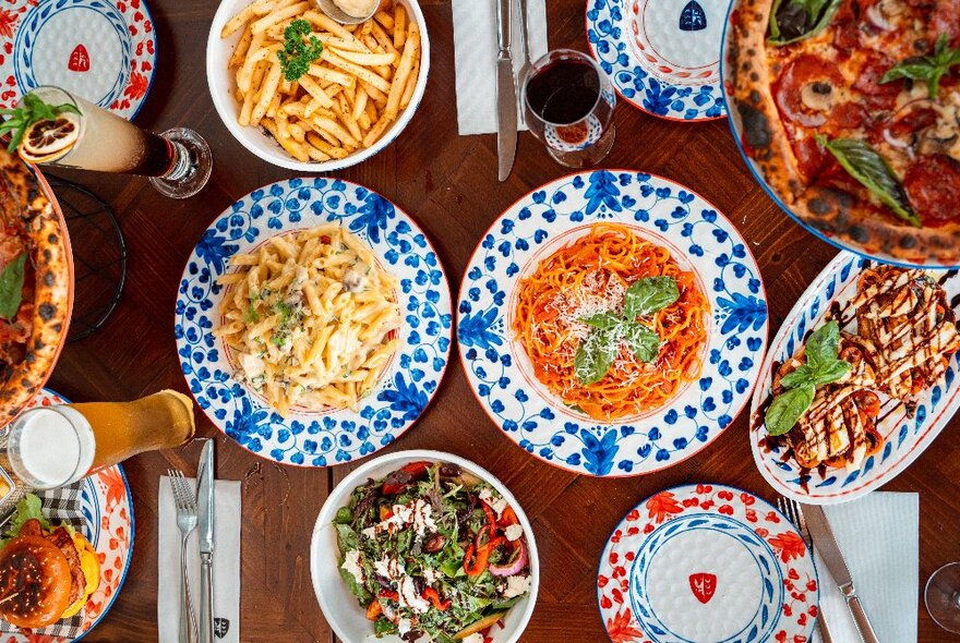 Colourfully decorated dishes of pasta and pizza on a wooden table.