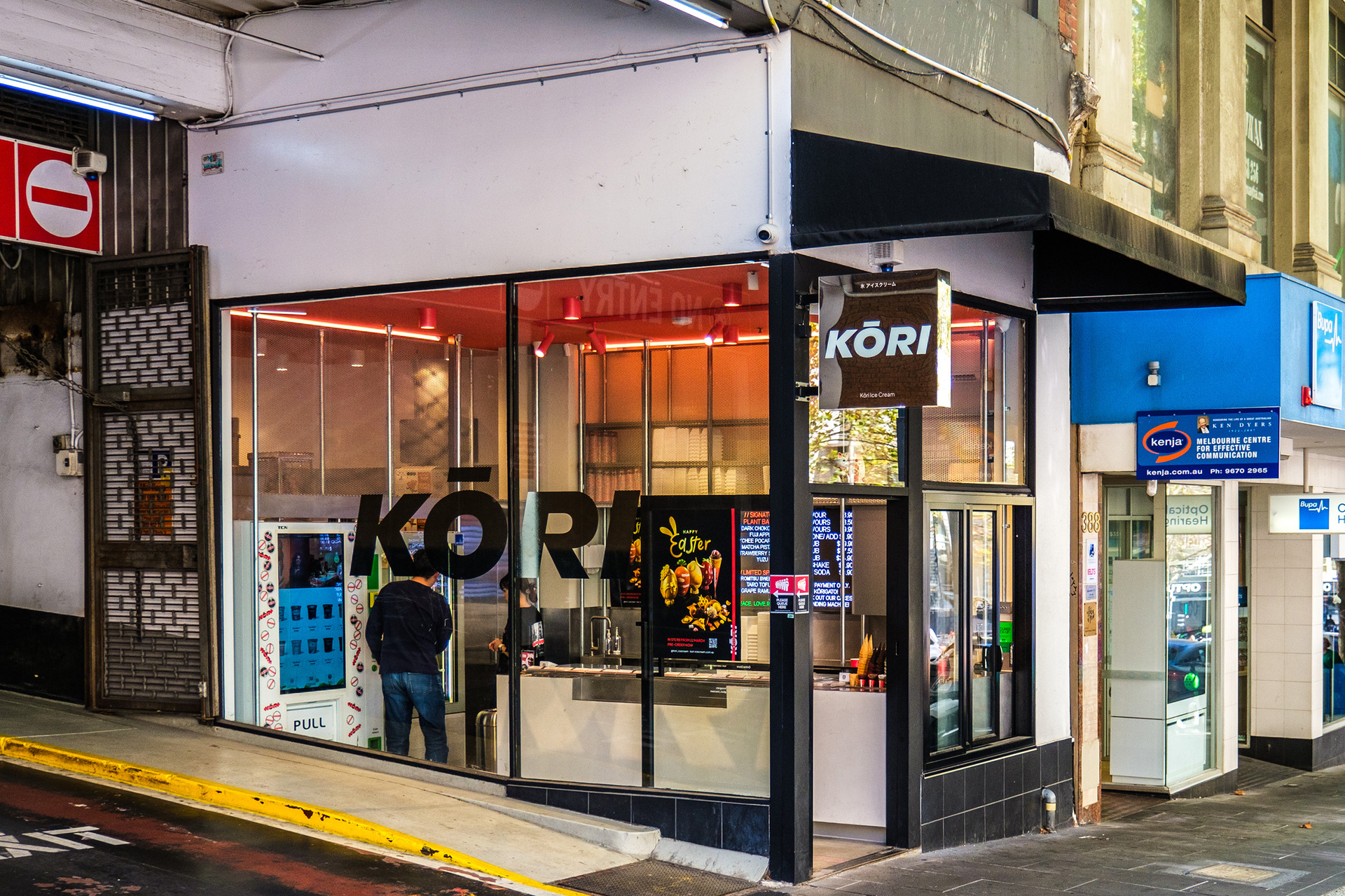 Outside a corner ice cream shop. There is a sign saying Kori and a customer is inside.