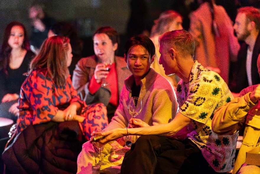 Friends socialising and chatting, with drinks in hand, in a large room at the NGV, at their Friday Nights events.