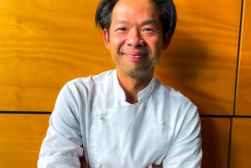 A smiling chef posing against a wall.