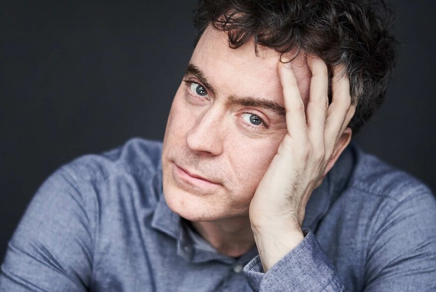 Pianist Paul Lewis, wearing a denim shirt with his head resting on his hand.