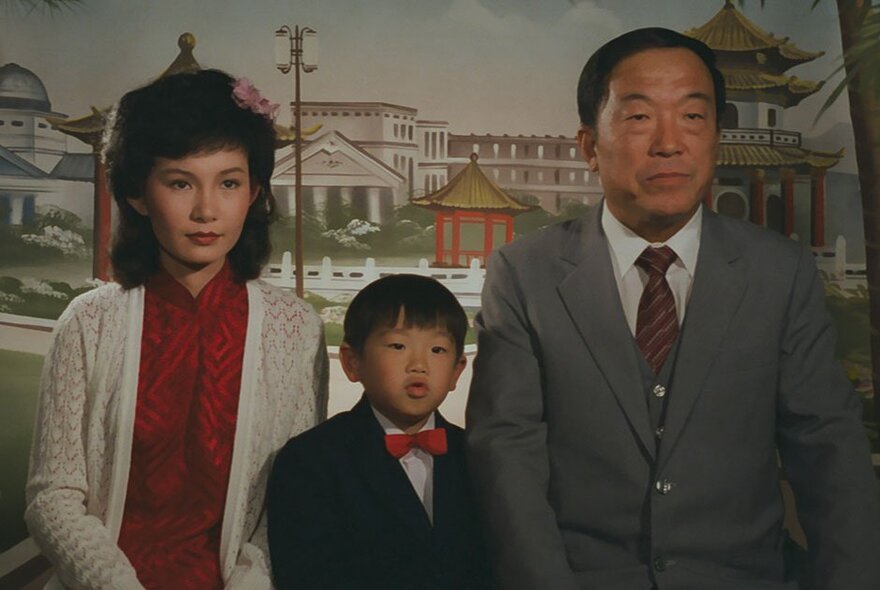 A still image from a Korean fulm showing a woman, man and young boy dressed up in formal clothes.