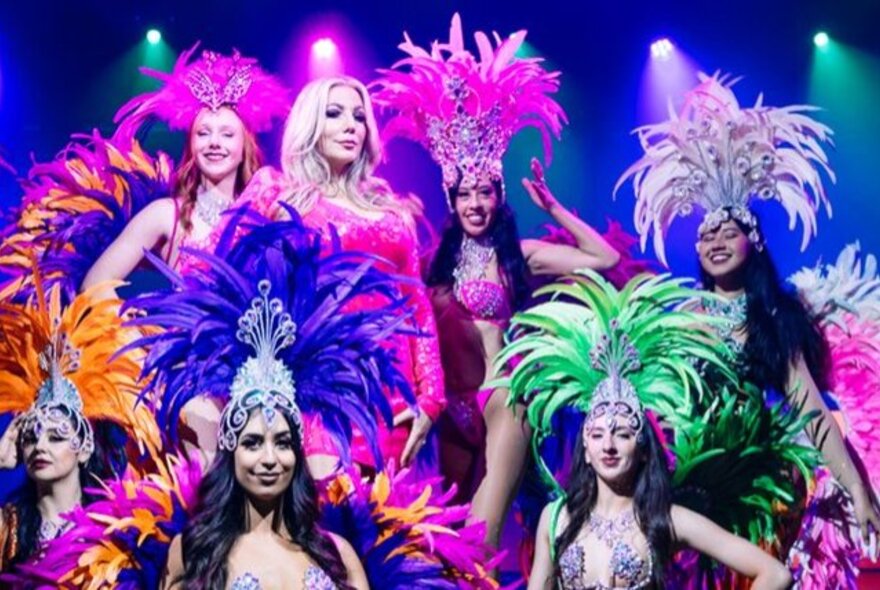 Showgirl performers wearing feathered headdresses under neon lights.