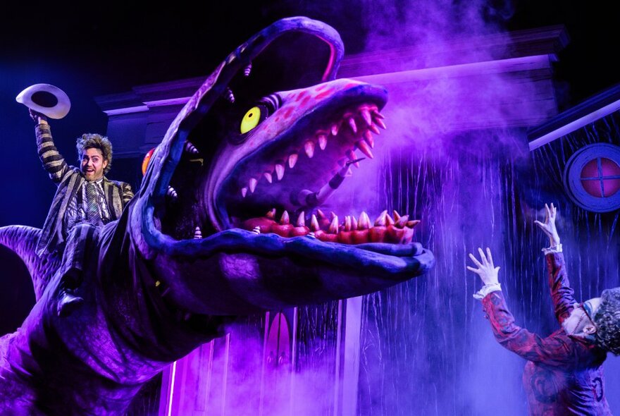 Cast member from  Beetlejuice The Musical, riding the head of a giant fish creature on a theatre stage. 