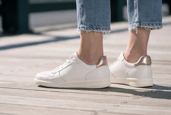 Person standing on a boardwalk wearing blue denim skinny jeans and white leather sneakers.