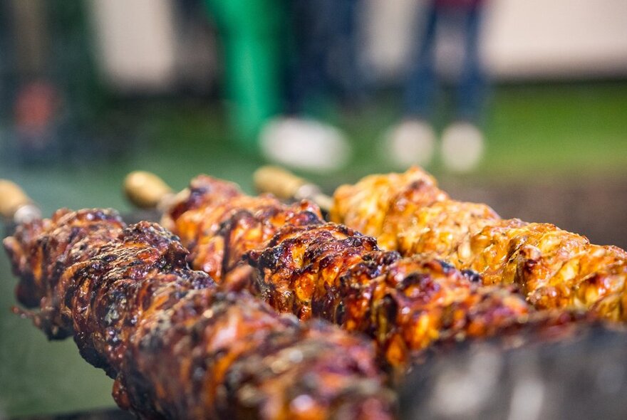 Three skewers of roasted meat on a barbecue.