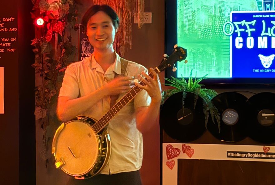 A smiling man with a banjo in front of a presentation screen inside a bar setting.