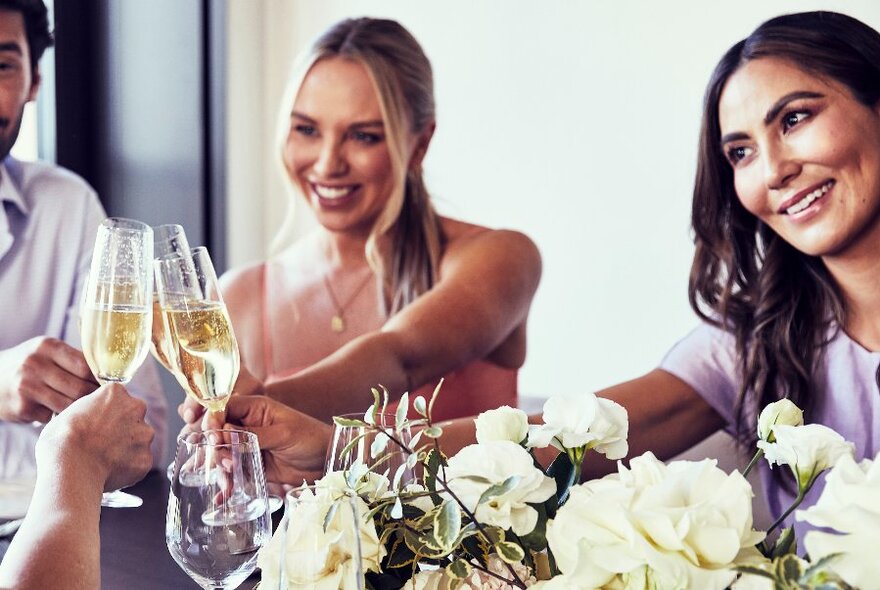 People clinking glasses of champagne over a floral table decoration.