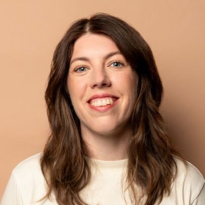 Portrait of comedian Alex Ward, smiling, with her long brown hair down past her shoulders.