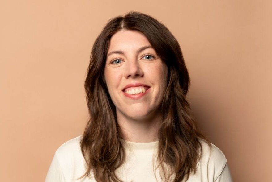 Portrait of comedian Alex Ward, smiling, with her long brown hair down past her shoulders.