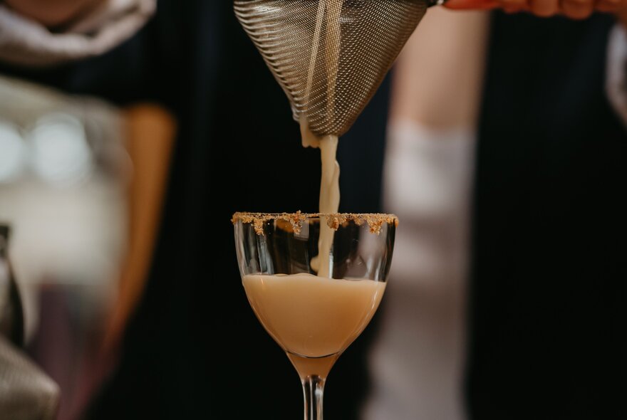 A cocktail being strained into a small glass with a coated rim. 