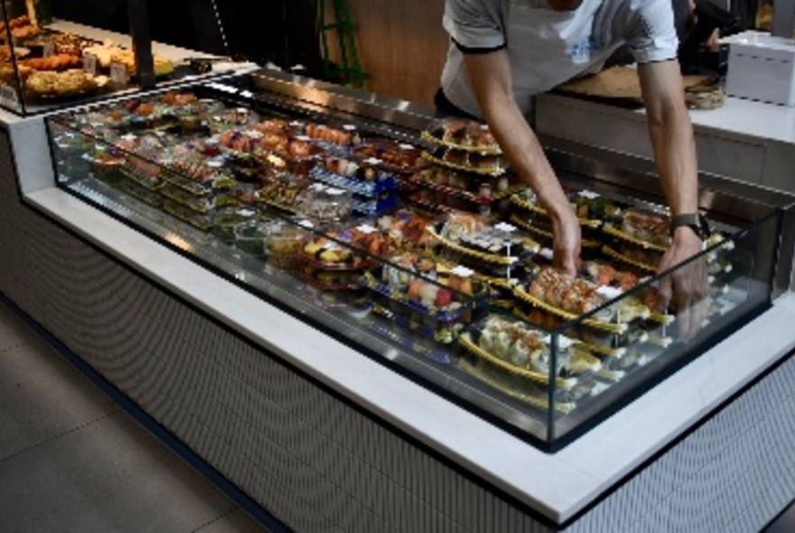 A staff member at Maki Roll placing trays of grab and go food trays into a food display counter.