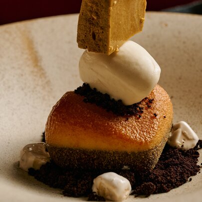 A Toblerone inspired dessert featuring a dark chocolate cremeux, honeycomb and nougat with a scoop of vanilla ice cream on a white plate