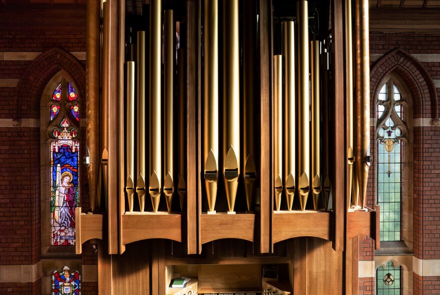 The pipes of a grand organ with stained glass windows around the sides. 