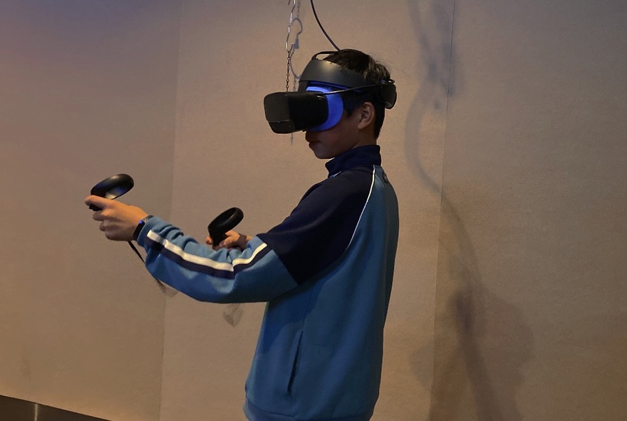 A player wearing a VR headset and using hand controls in a room.