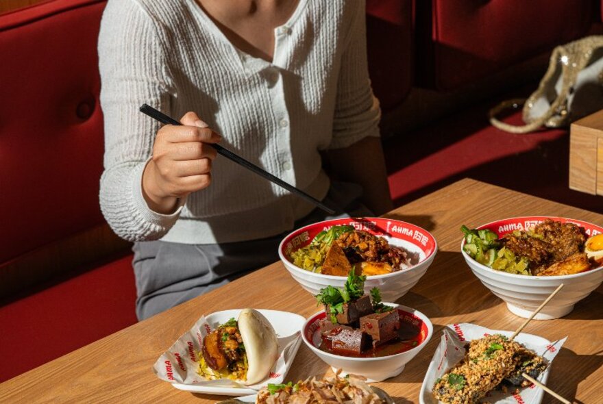 A headless diner about to dive a chopstick into a bowl of Taiwanese food, with many plates of different dishes on the table. 