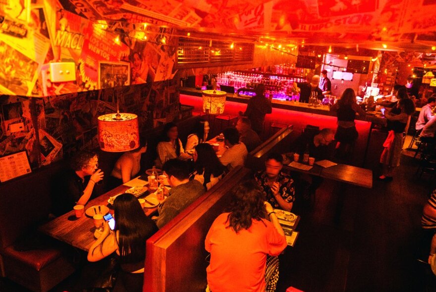 Underground Mexican restaurant with a dimly lit glowing red interior, funky wallpaper and lots of customers drinking and dining.