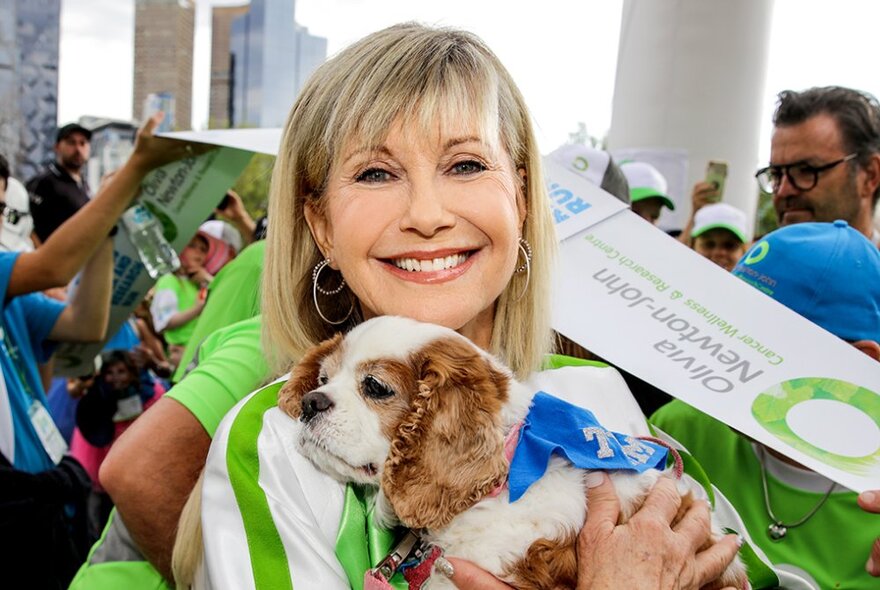 Olivia Newton-John holding a spaniel puppy with blue ribbon.