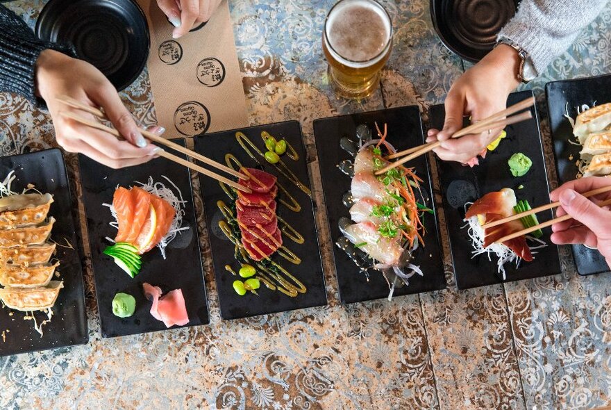 People using chopstics to eat a range of Japanese dishes on small plates.