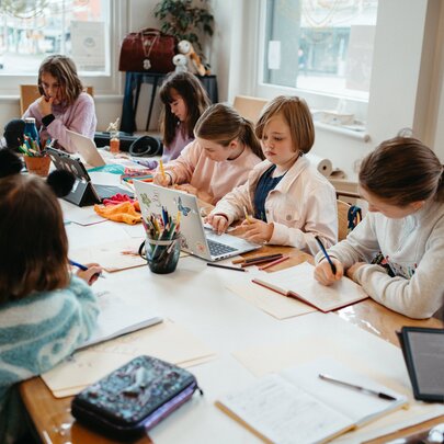 Kids seated around a large table writing and drawing during a creative writing workshop in a bright studio space.