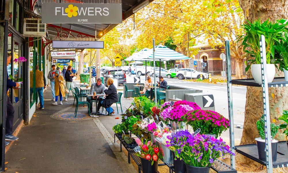 People dining on a city strip with a flower display outside a florist.