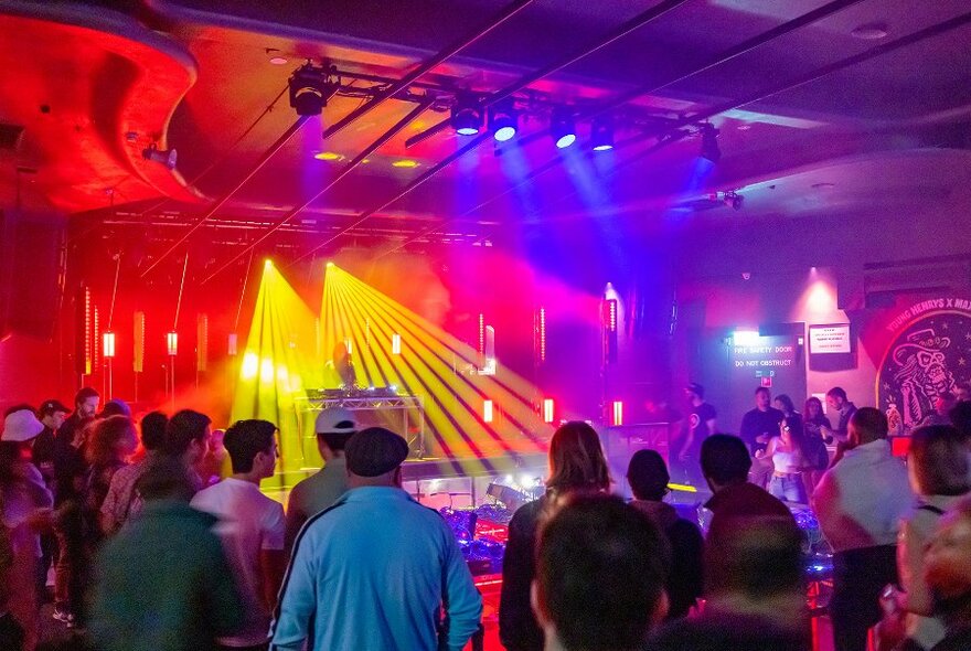 Crowds watching a gig under rainbow lighting.