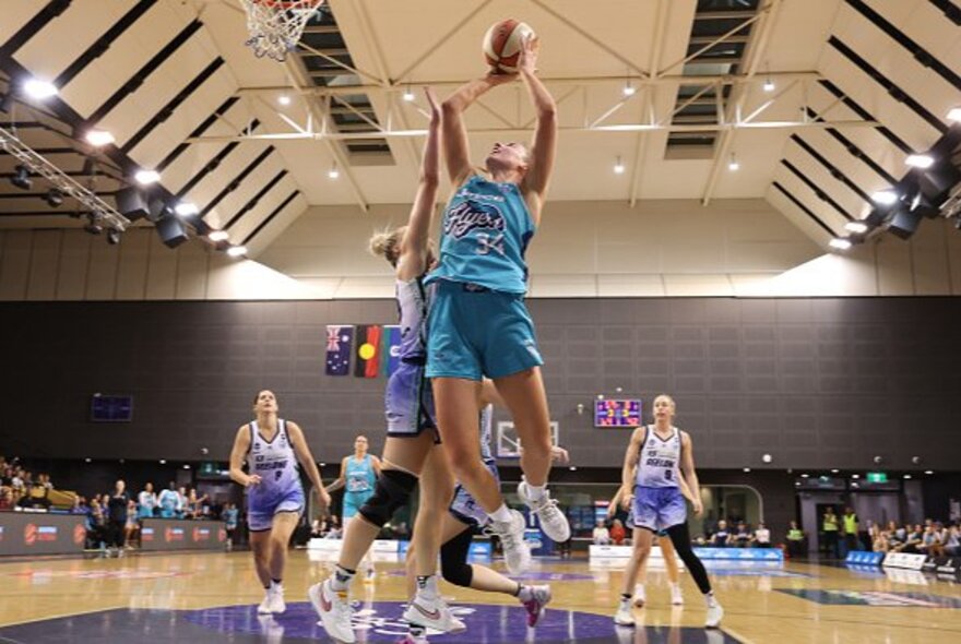 Female basketballers scoring and defending a goal in an indoor stadium.