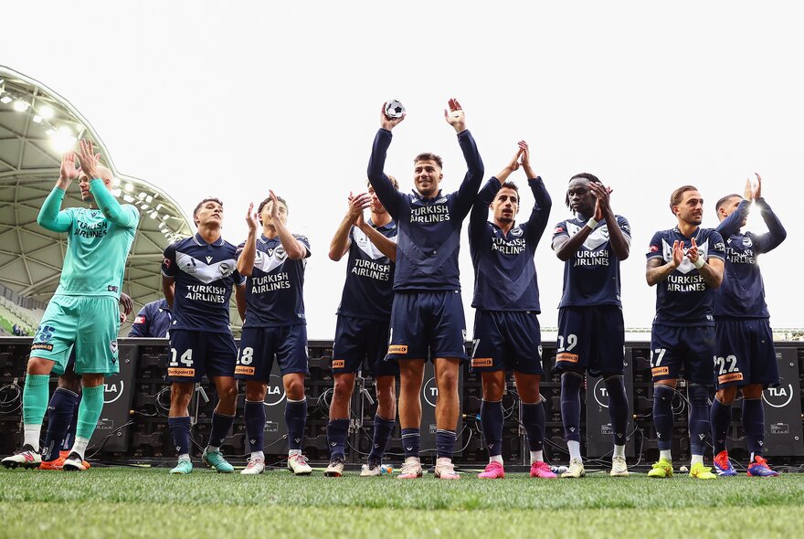 Soccer players applauding with a referee on the left.