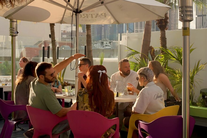 People enjoying drinks and socialising on the Palmz rooftop bar at The Carlton Club, with city buildings in the distance.