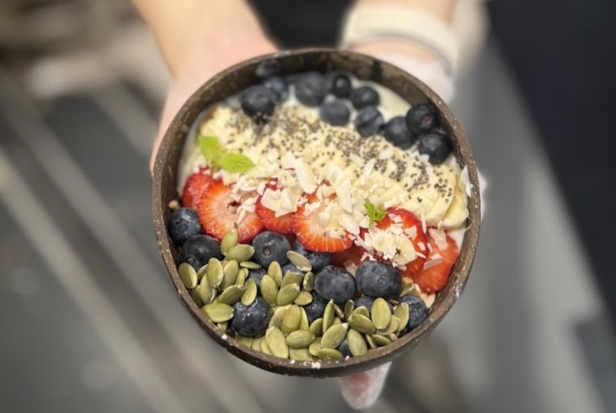 Hands holding a breakfast bowl with fruit and seeds.