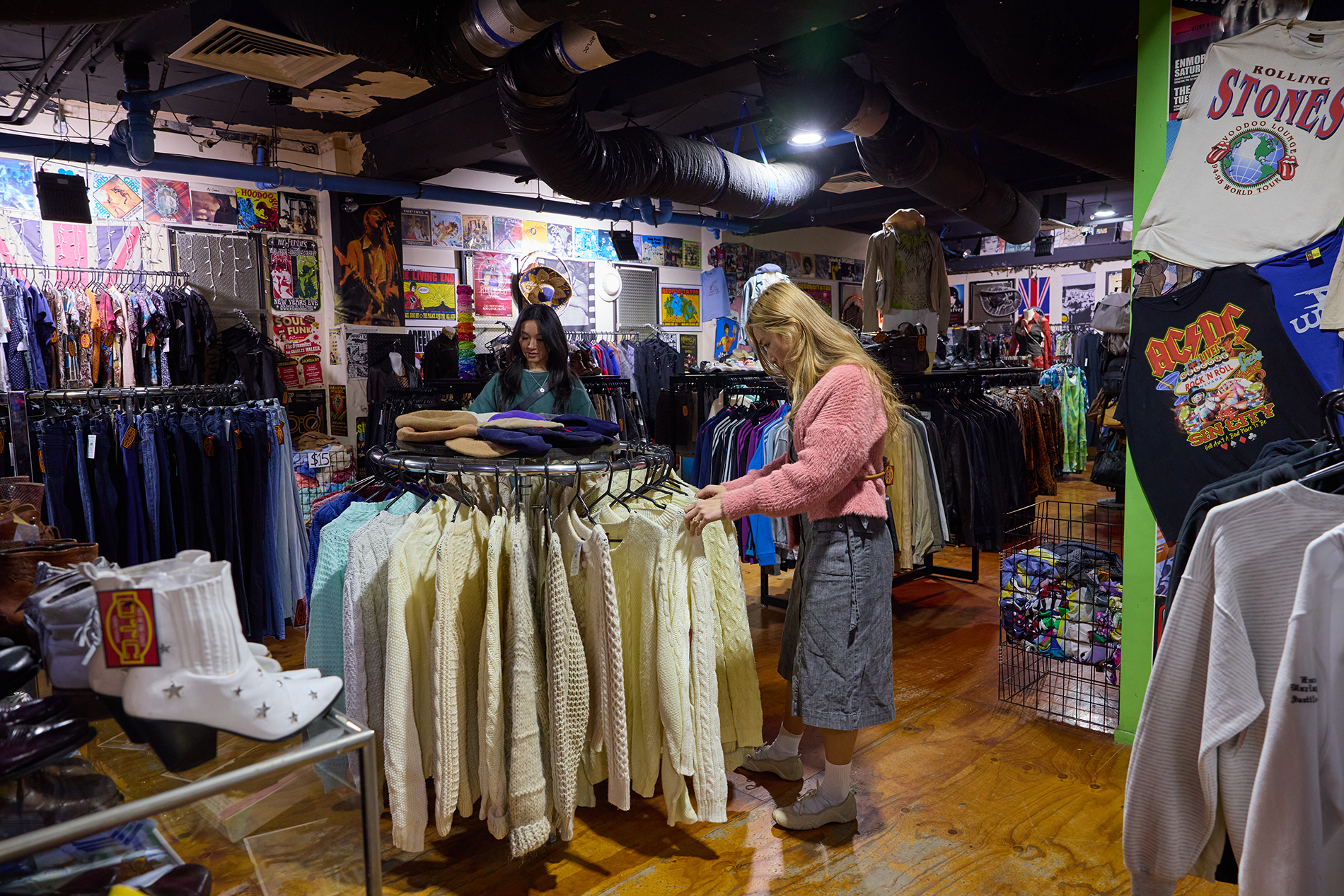 Two girls browsing a rack of cream cable knit jumpers in an op shop.