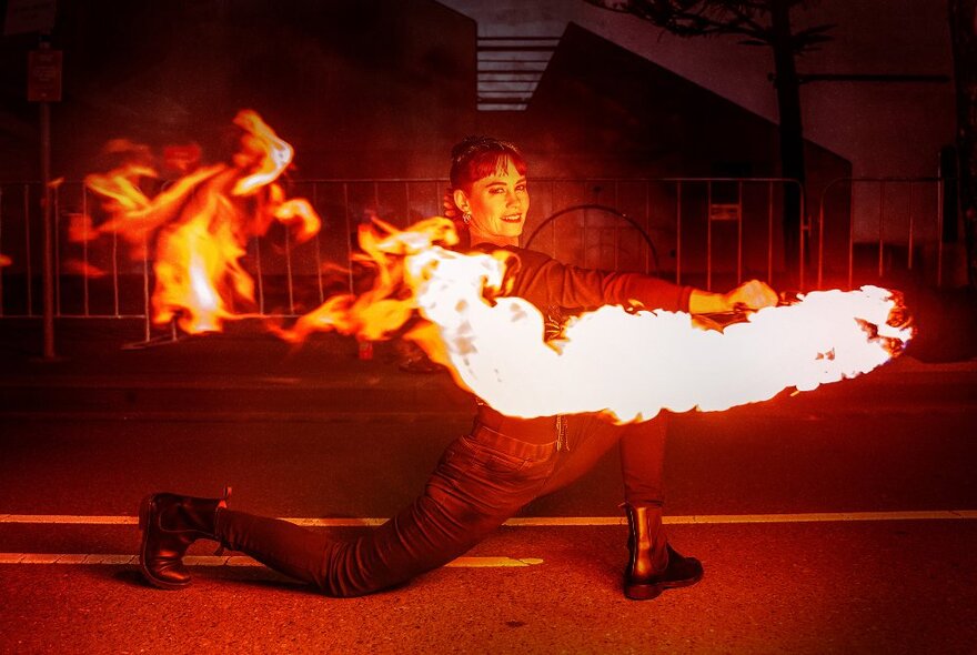 A fire twirler performing outdoors at night at the Firelight Festival.