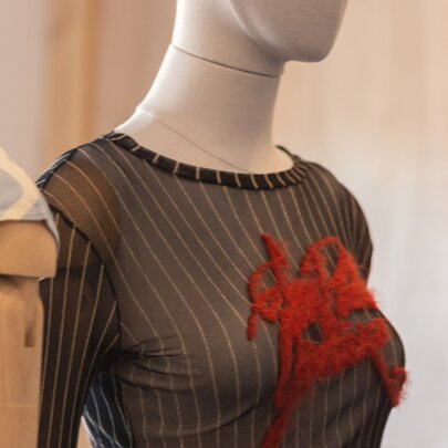A vintage sheer mesh long-sleeve top featuring black-and-grey vertical pinstripes and a red graphic applique across the chest, worn on a mannequin.