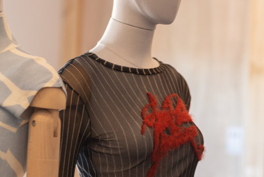 A vintage sheer mesh long-sleeve top featuring black-and-grey vertical pinstripes and a red graphic applique across the chest, worn on a mannequin.