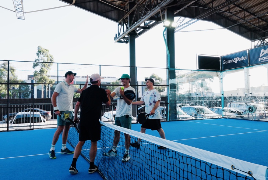 Four people chatting over a net on a padel court. 