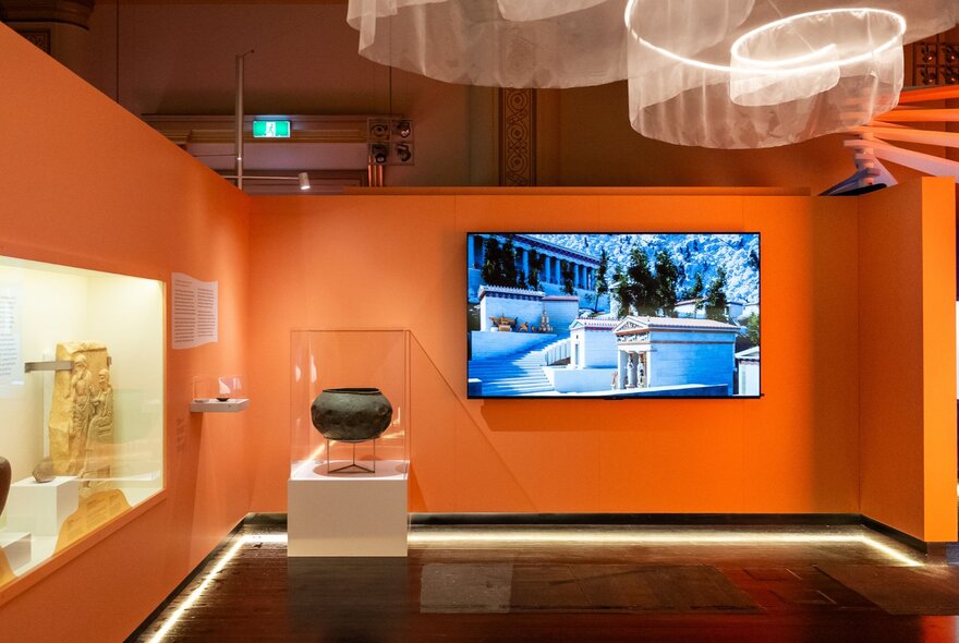 An exhibition installation in a room with orange walls at the Hellenic Museum.