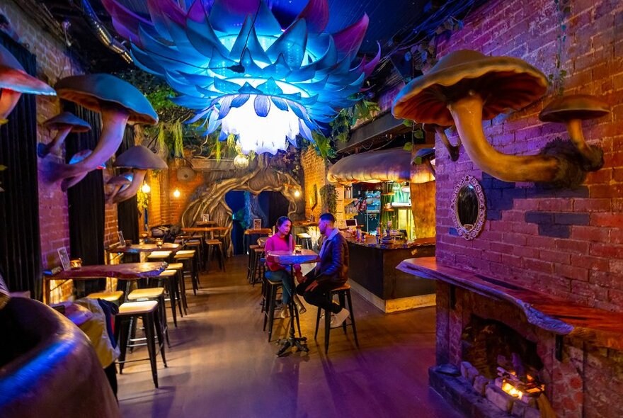 A couple in a bar surrounded by giant mushrooms.