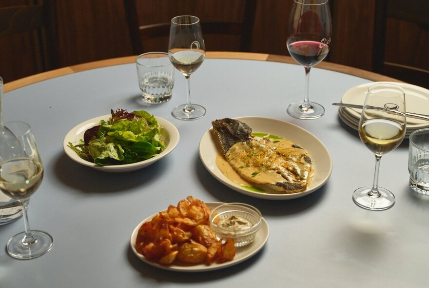 A restaurant table set with wine, a whole fish, salad and potatoes.