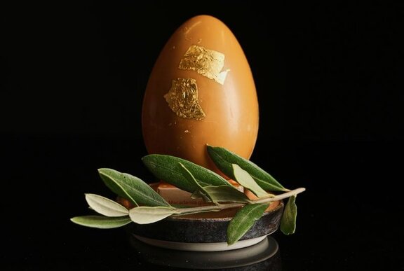 A large caramel chocolate egg with 24 karat gold leaf, resting on a small platter with a sprig of a native Australian bush.