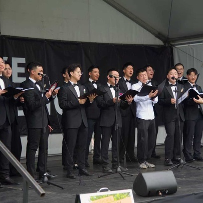 The True Colours male choir performing in formal black suits with bow ties on a covered  outdoor stage.