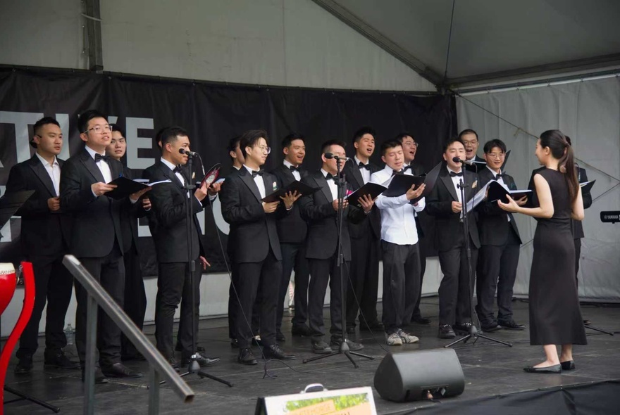 The True Colours male choir performing in formal black suits with bow ties on a covered  outdoor stage.