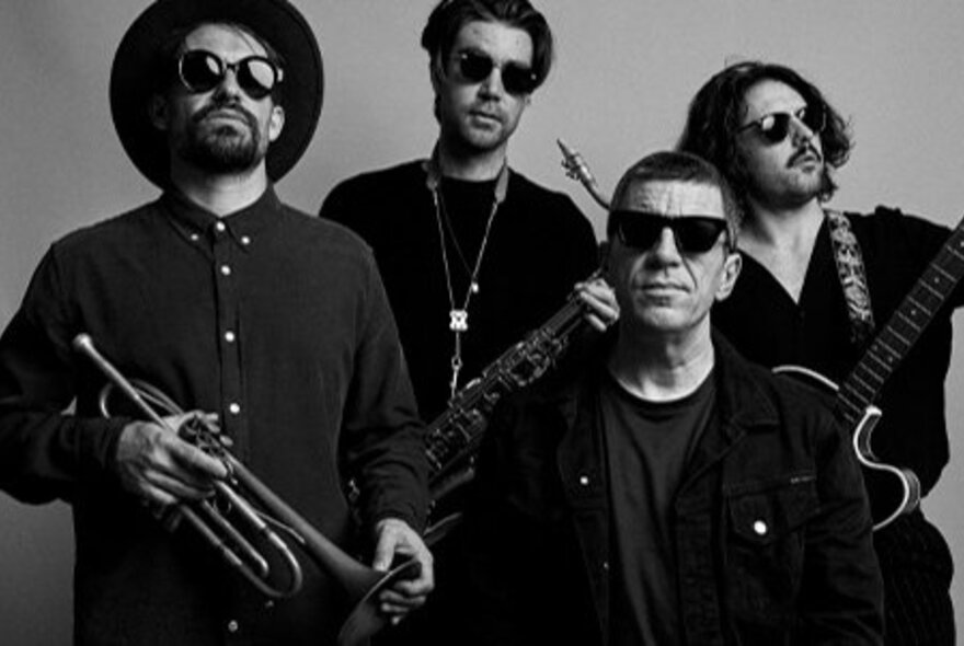 The four male members of the band The Vampires posing for a group photo, all wearing dark shirts and sunglasses, three of them holding their instruments.