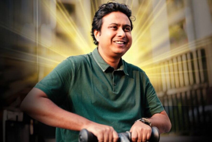 Comedian Anirban Dasgupta, smiling in a green polo shirt with a glowing beam around him. 