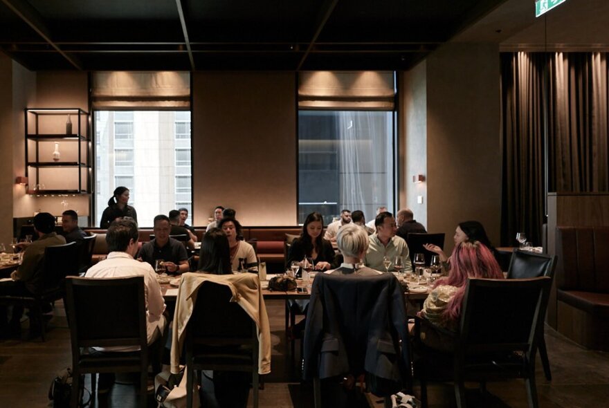 People eating and drinking at tables in La Madonna restaurant, with soft lighting and large windows on the rear wall.