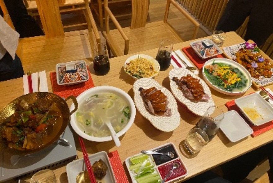 A selection of Chinese food, including Peking Duck, a hot pot and other delicious dishes, on a wooden table.